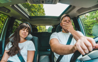 a man driving while yawning with a woman sleeping in the passenger seat