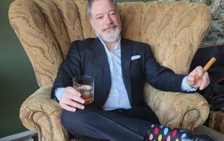 Spencer smoking a cigar with a drink in hand