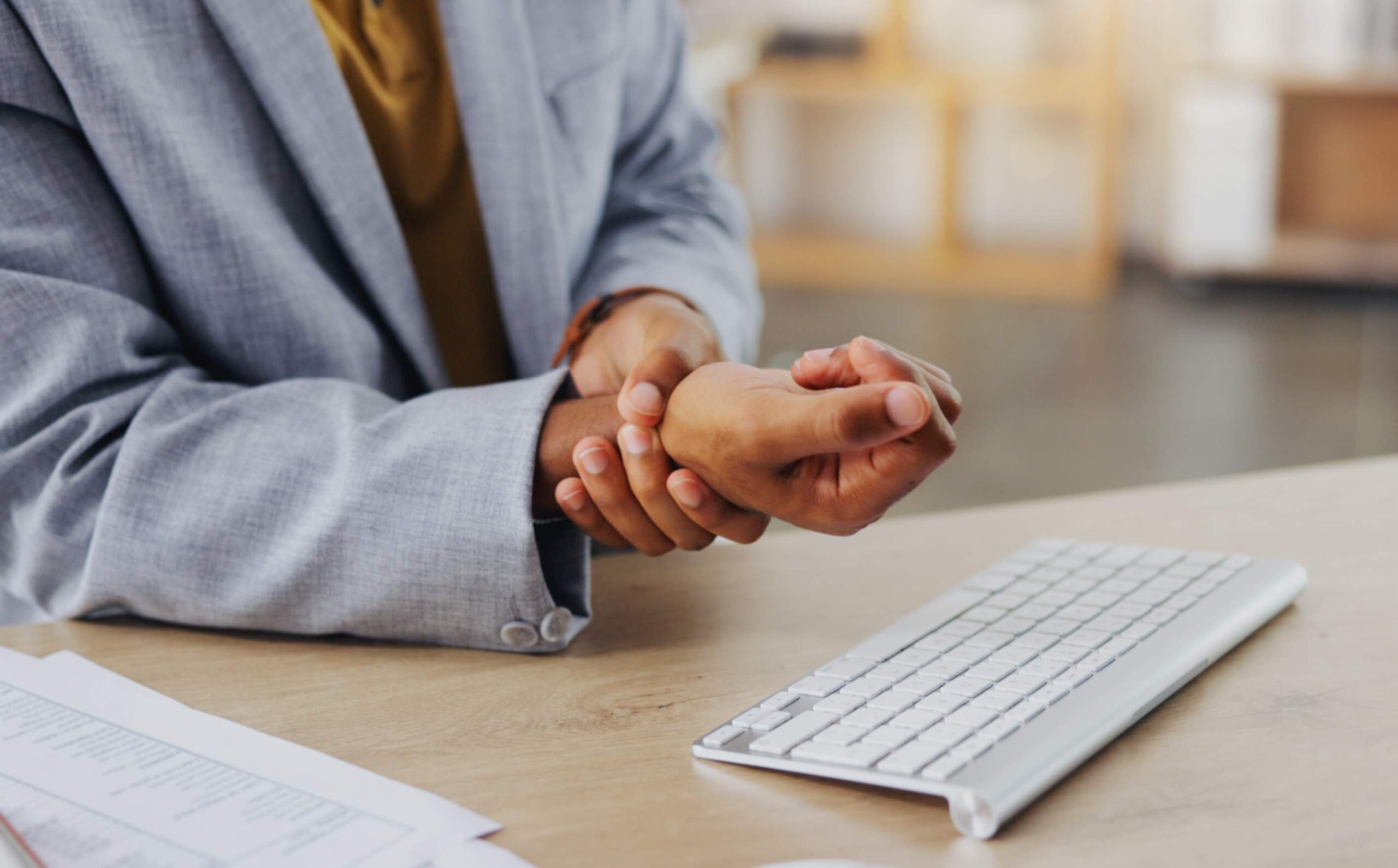 Person experiencing wrist pain while working at a desk with a computer keyboard, illustrating common workplace injuries related to repetitive motion.