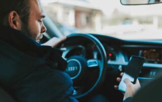 Man driving an Audi while looking at a smartphone, illustrating the dangers of texting and driving related to car accidents in Missouri.